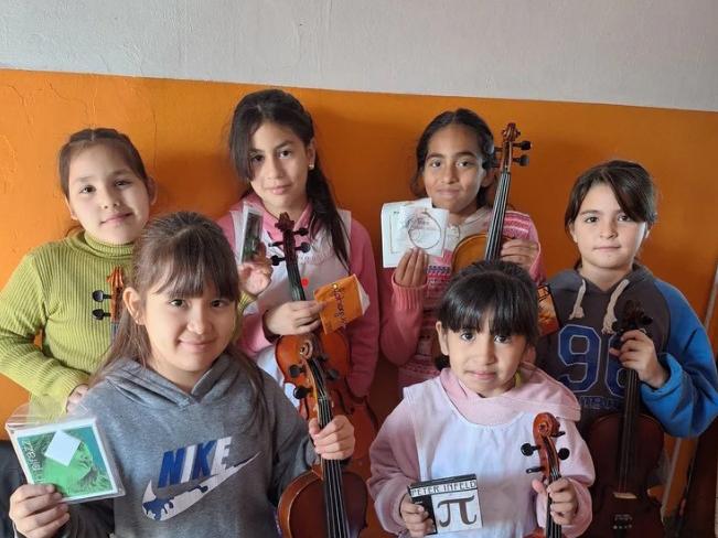 Six young South American children posing with string instruments and packs of strings