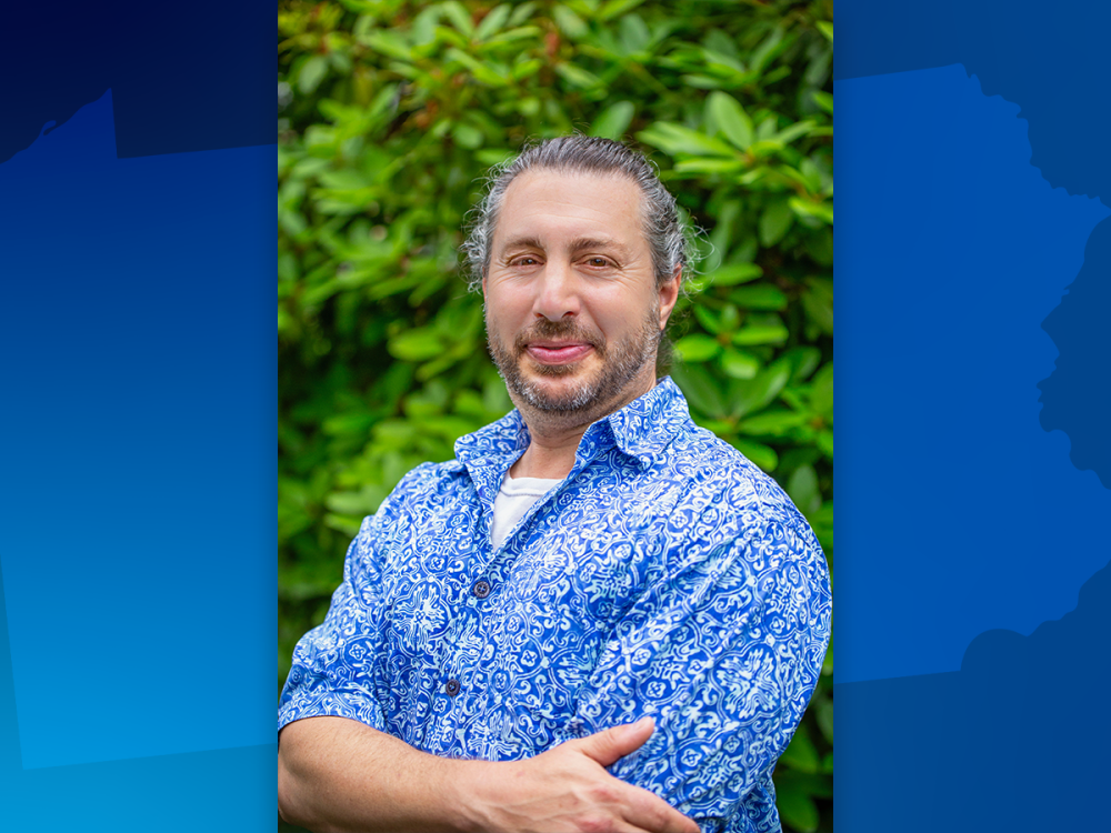 Michael Vicaro posing in front of shrubbery.