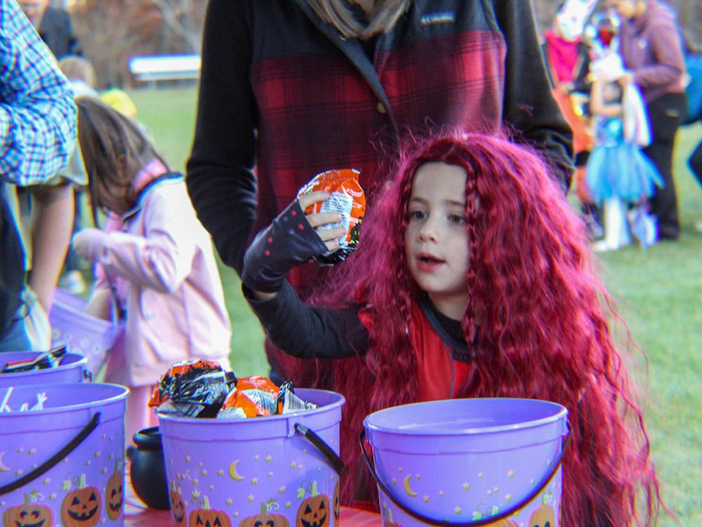 A child in a costume with a red wig and a candy bag.