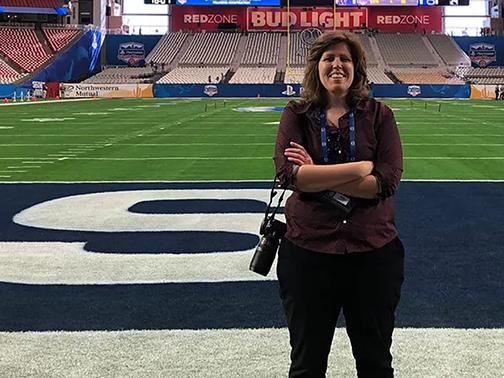 Woman with arms crossed standing on a football field with a camera around her neck