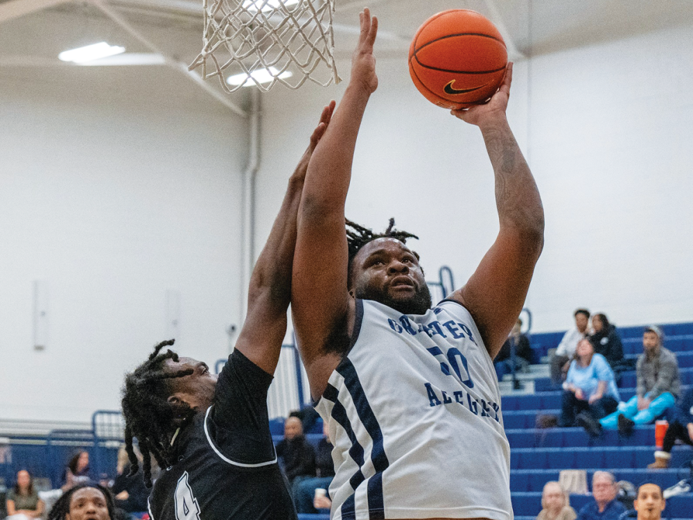 Bryce Phillips, wearing a Penn State Greater Allegheny jersey, jumps toward the basket while holding a basketball during a game as an opposing player defends.