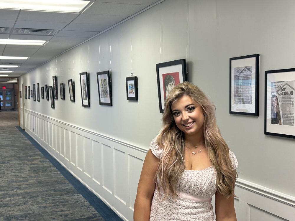 Bryna Brinkman stands in front of her artwork displayed in Olmsted Building at Penn State Harrisburg