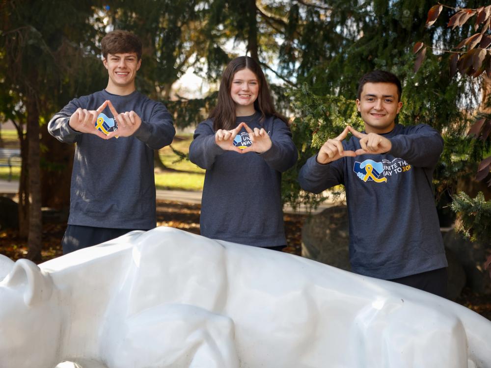 Joey Pretti, Morgan Gallagher and Charles Carlini with their hands shaped as the four diamonds logo behind the lion