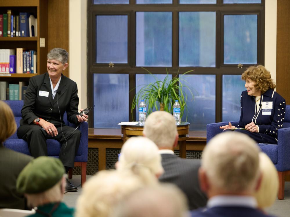 two seated women talking in front of crowd