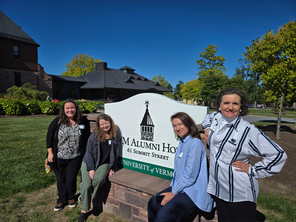 Four women pose outdoors beside a sign reading “UVM Alumni House, 61 Summit Street, The University of Vermont.” They are among the Penn State participants at the inaugural University of Vermont Center for Community News (CCN) Conference, which brought together more than 130 journalism professionals, educators, and advocates.