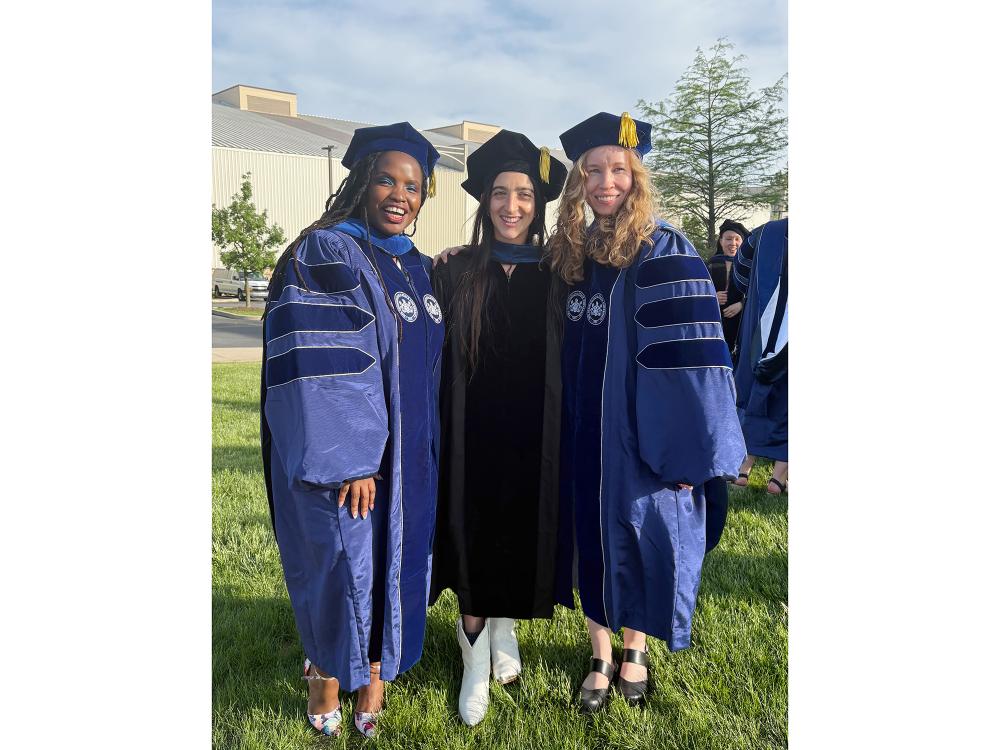 Three doctoral graduates wearing academic graduation robes and tams