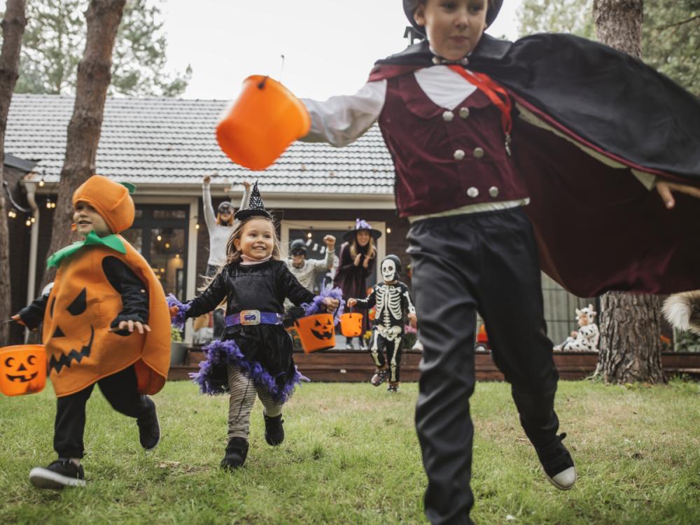 A group of children in Halloween costumes runs through the back yard of a home.