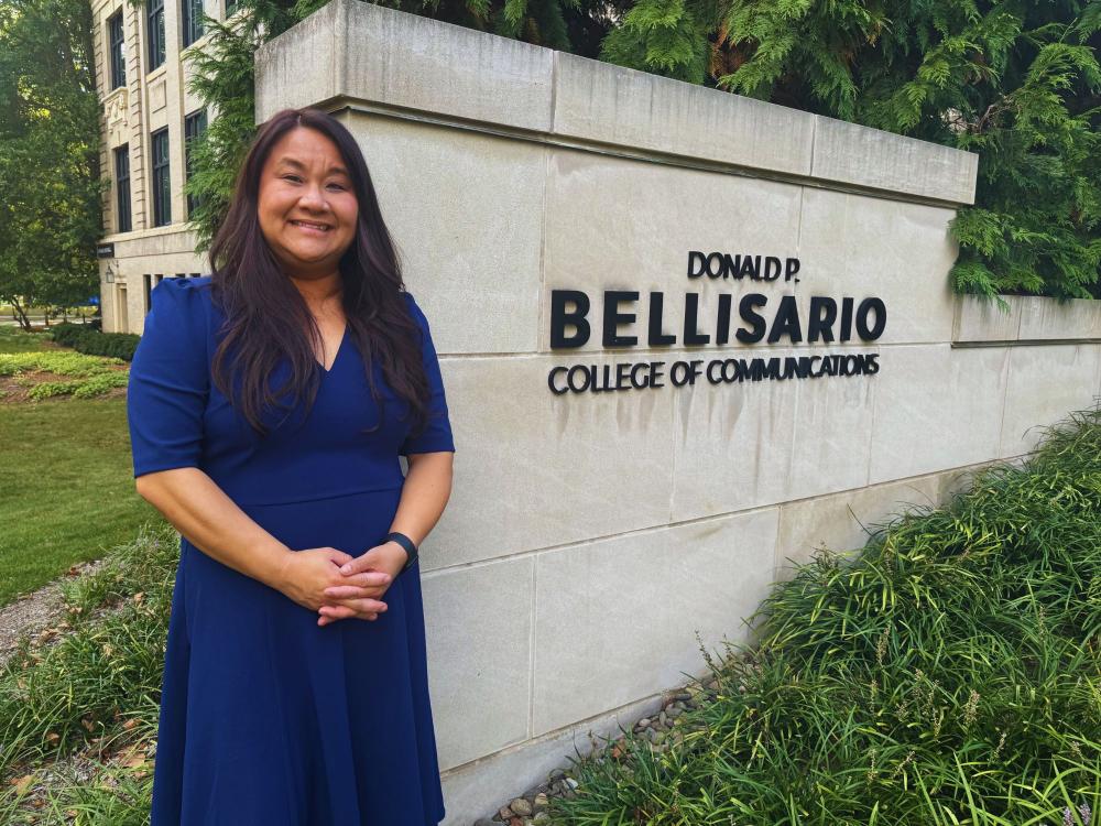 Holly Overton stands in front of a cement wall that reads "Donald P. Bellisario College of Communications"