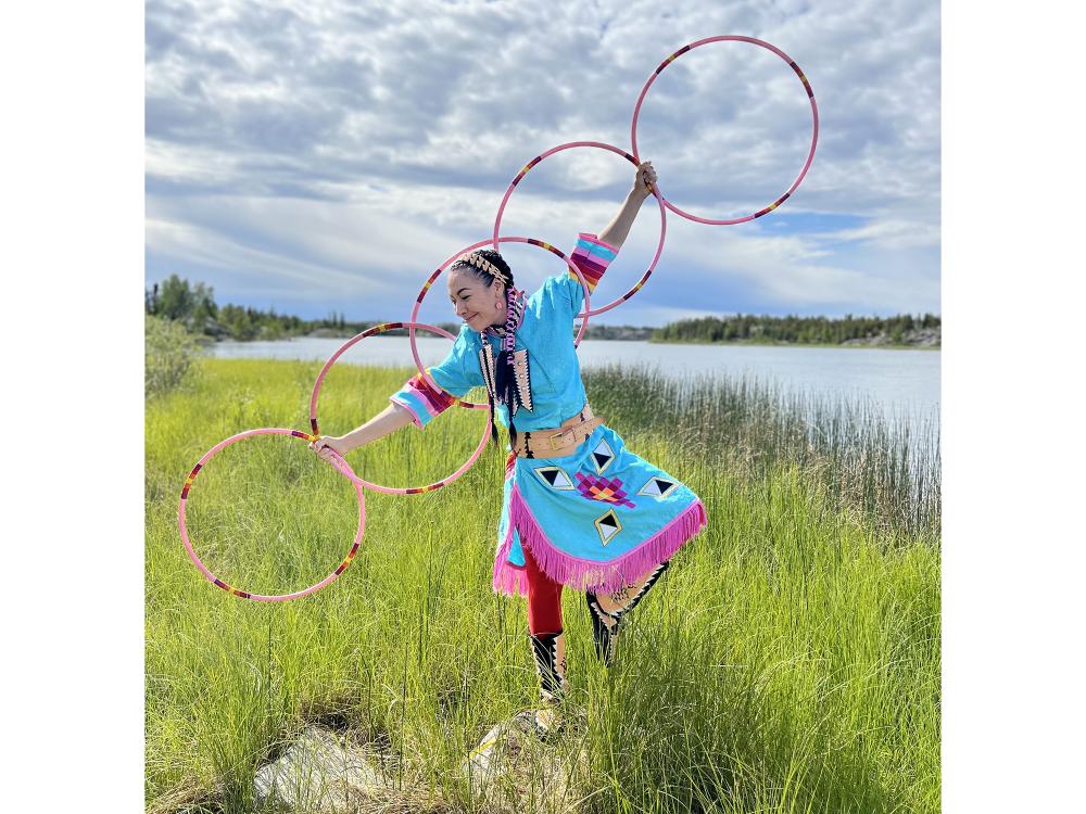 A dancer playing with hoops in a field against a bright blue sky