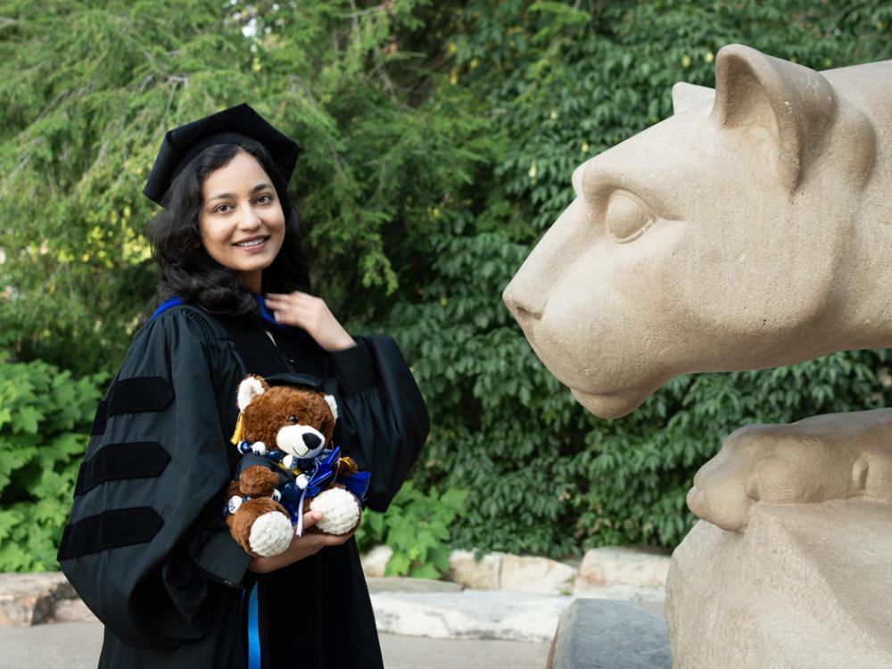 Sana Ahrar in graduation garb standing next to the Nittany Lion Shrine.
