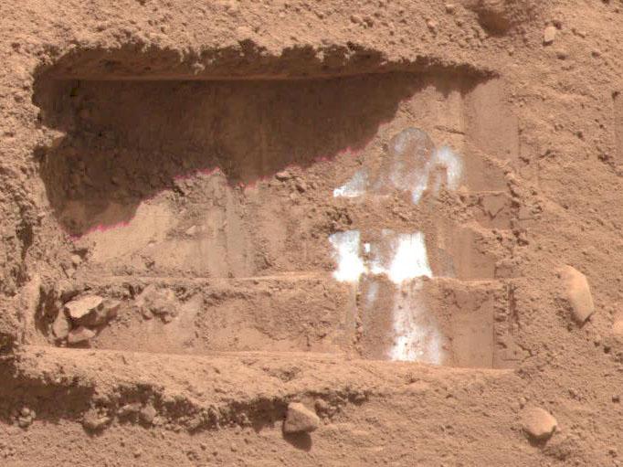 Reddish Martian soil is seen with flecks of Martian ice.