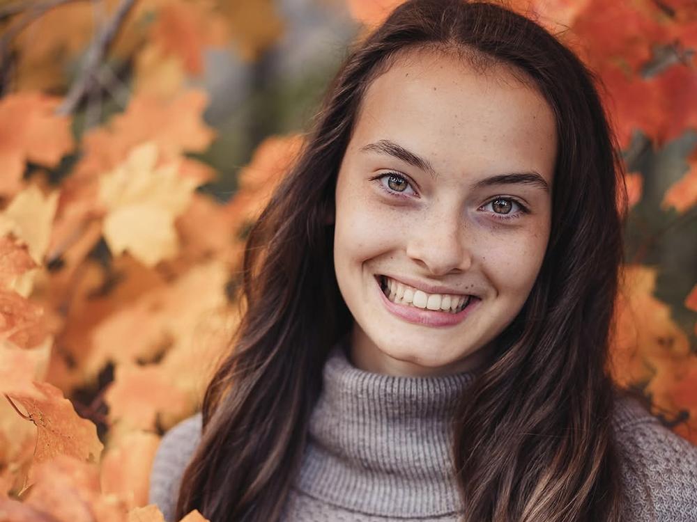 Portrait of Maya Bergman wearing gray sweater among fall leaves