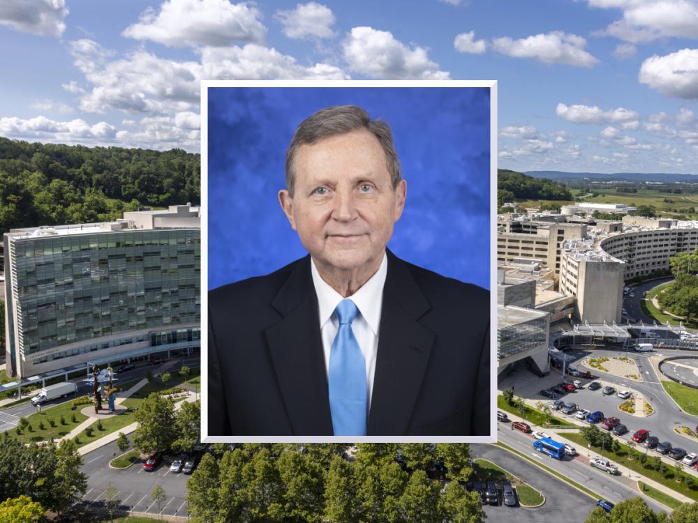 A professional headshot photo of Dr. Robert Harbaugh wearing a suit and tie is superimposed over an image of Milton S. Hershey Medical Center.