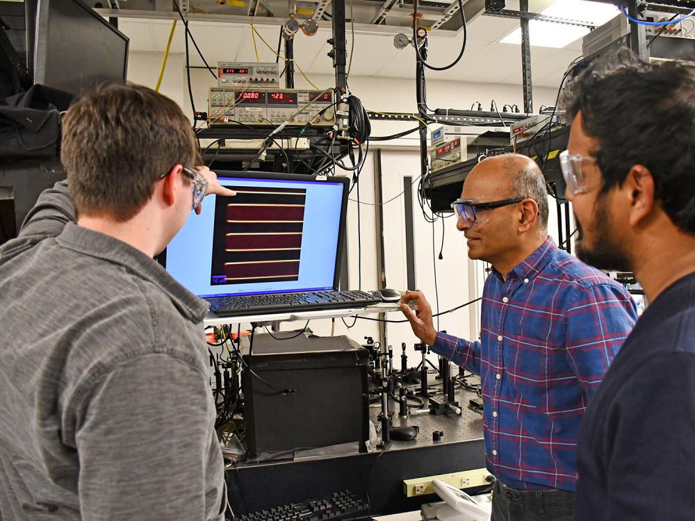 Three researchers look at a computer screen in a lab