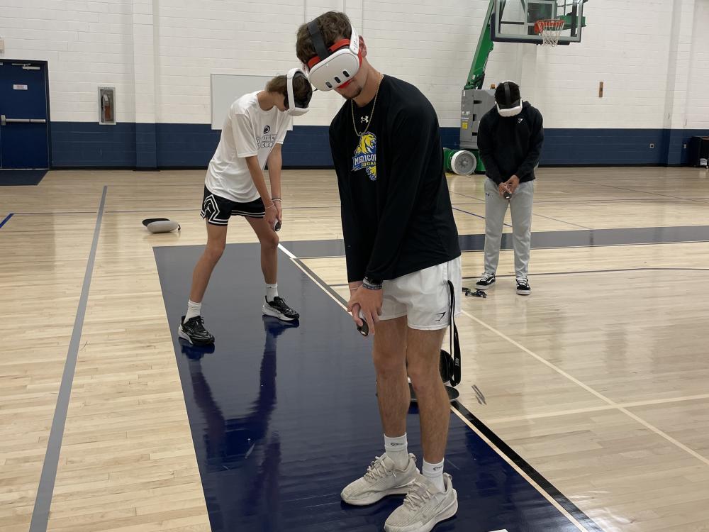 Three students wearing virtual reality headsets in gymnasium