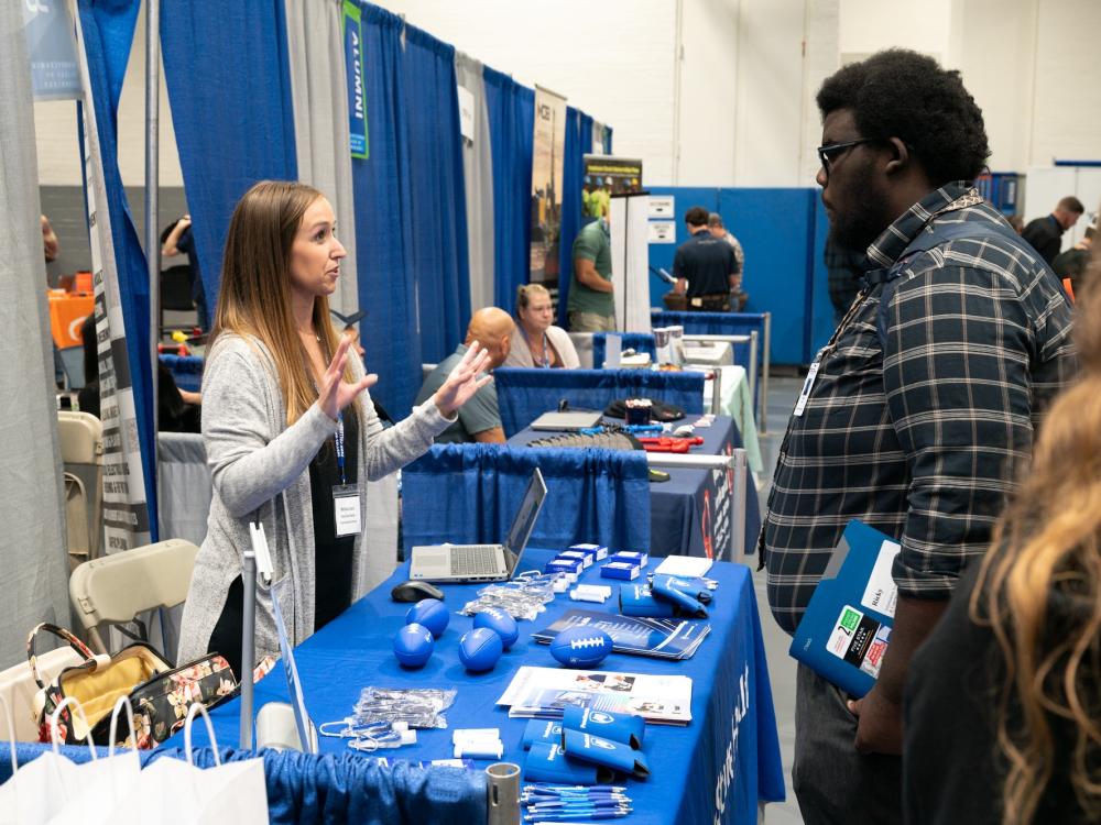 A recruiter and a student talk at a table during the Penn College Fall 2025 Career Fair.