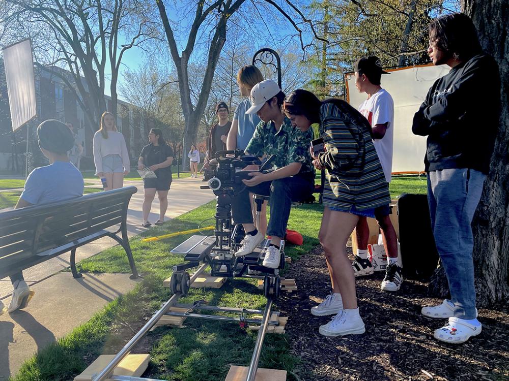 Students crowd around a camera during an on-location film shoot