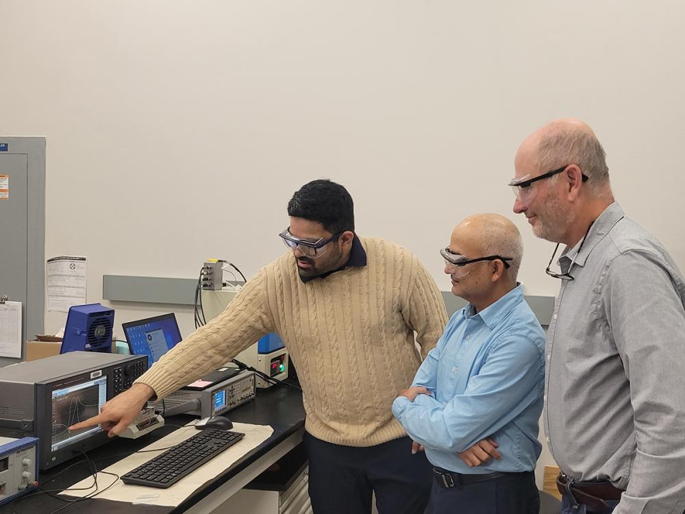 Three individuals look toward a computer 
