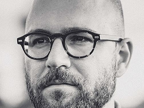 Upclose image of a bearded, balding man with round-framed glasses