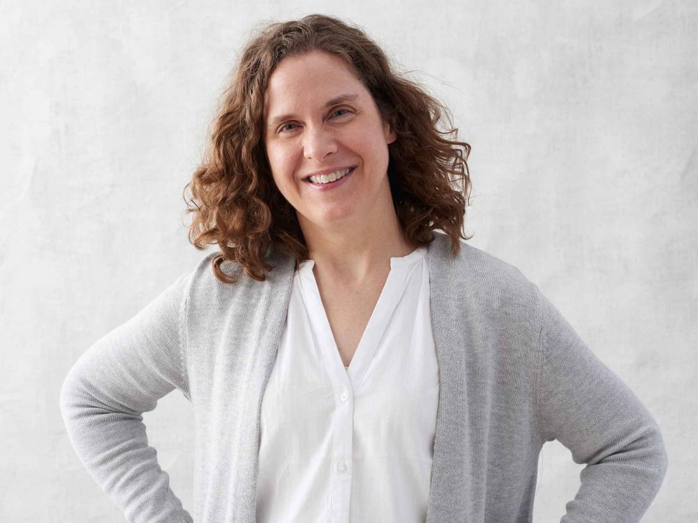 smiling woman wearing blouse and sweater, with her hands on her hips