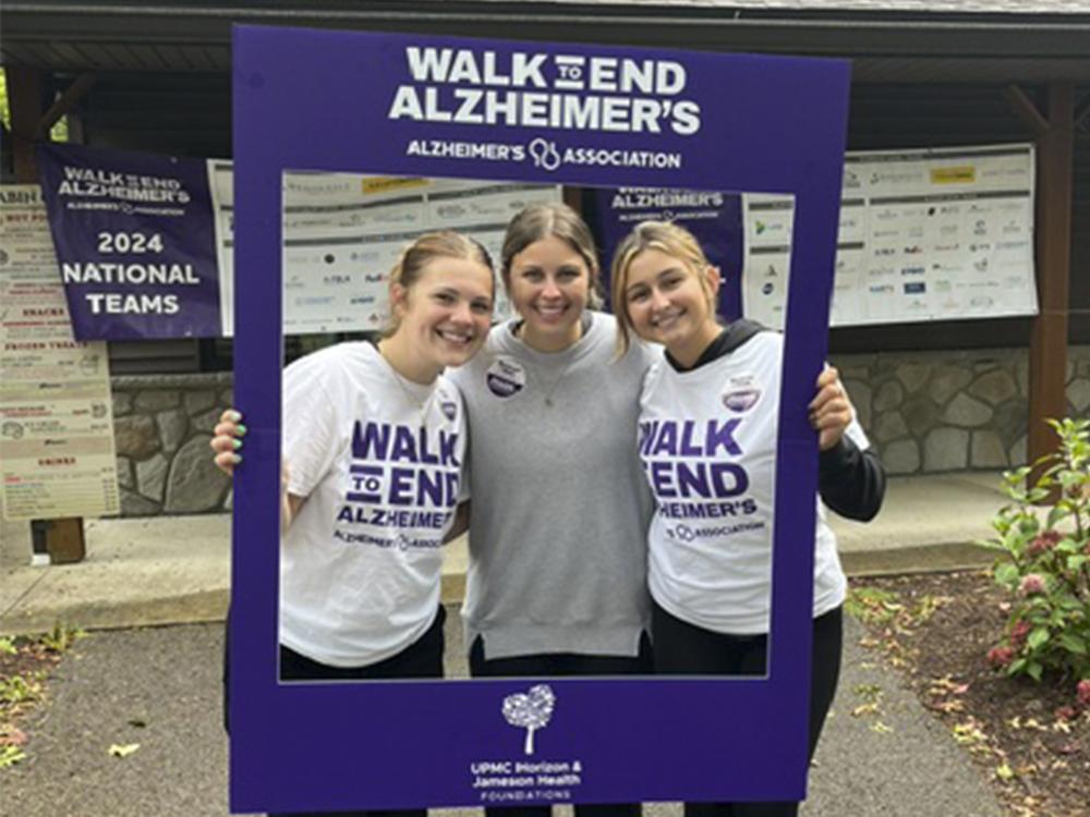 Three students pose for a photo while holding a purple Walk to End Alzheimer's selfie frame.