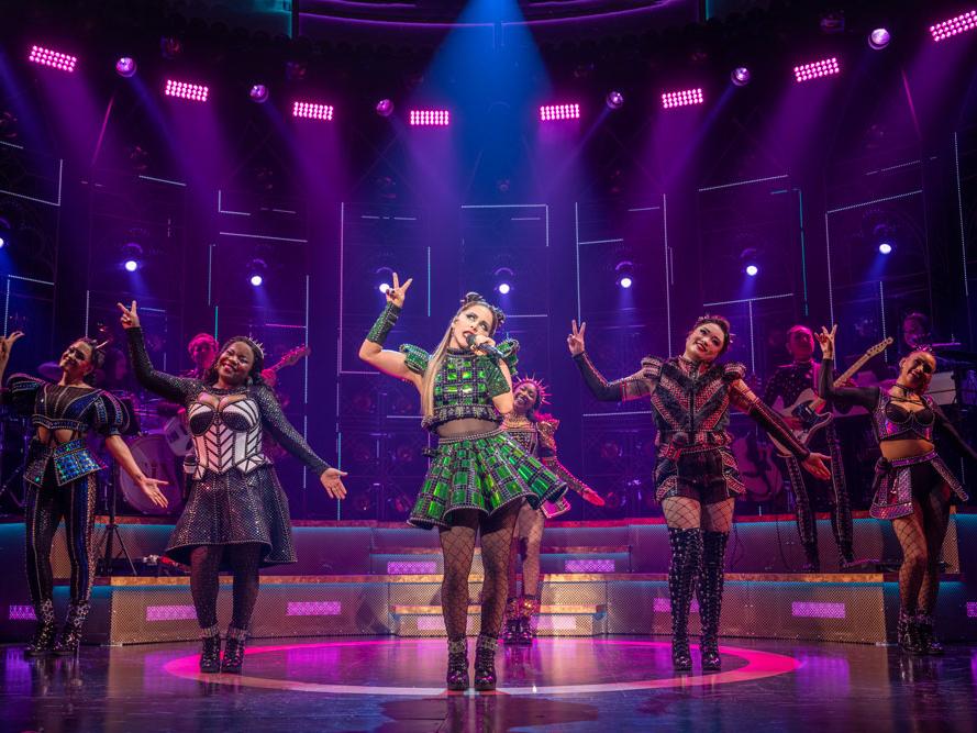 A cast of diverse women wearing stylized Tudor costumes sing in unison.