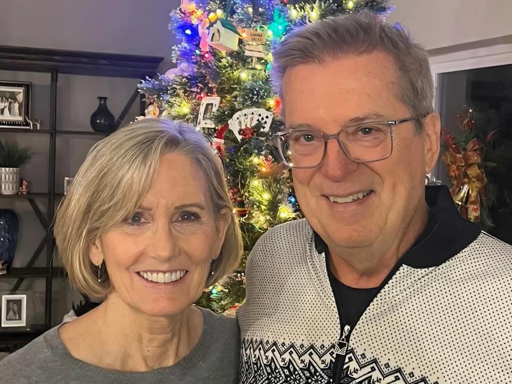 A photo of Suzanne Watson and Brian Dreckshage smiling and standing in front of a Christmas tree.