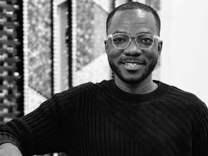 Black and white image of a Black man with clear rimmed glasses smiling