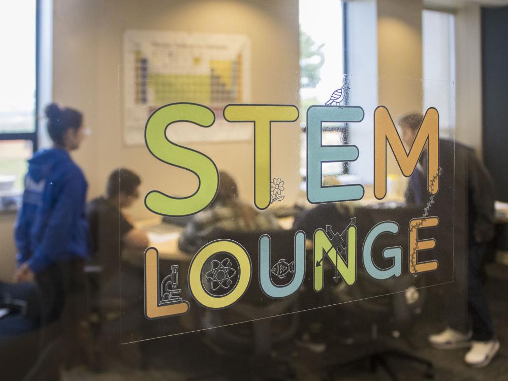 A view through a glass window of students gathered inside the new STEM Lounge