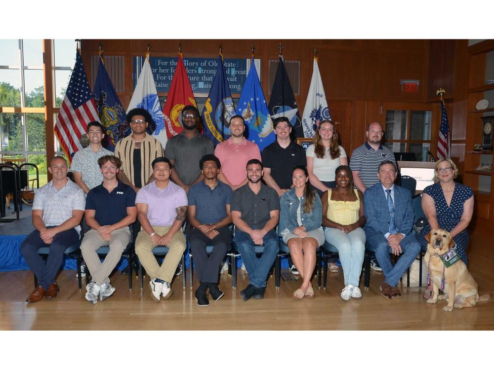 Two rows of people standing in front of flags and smiling at the camera