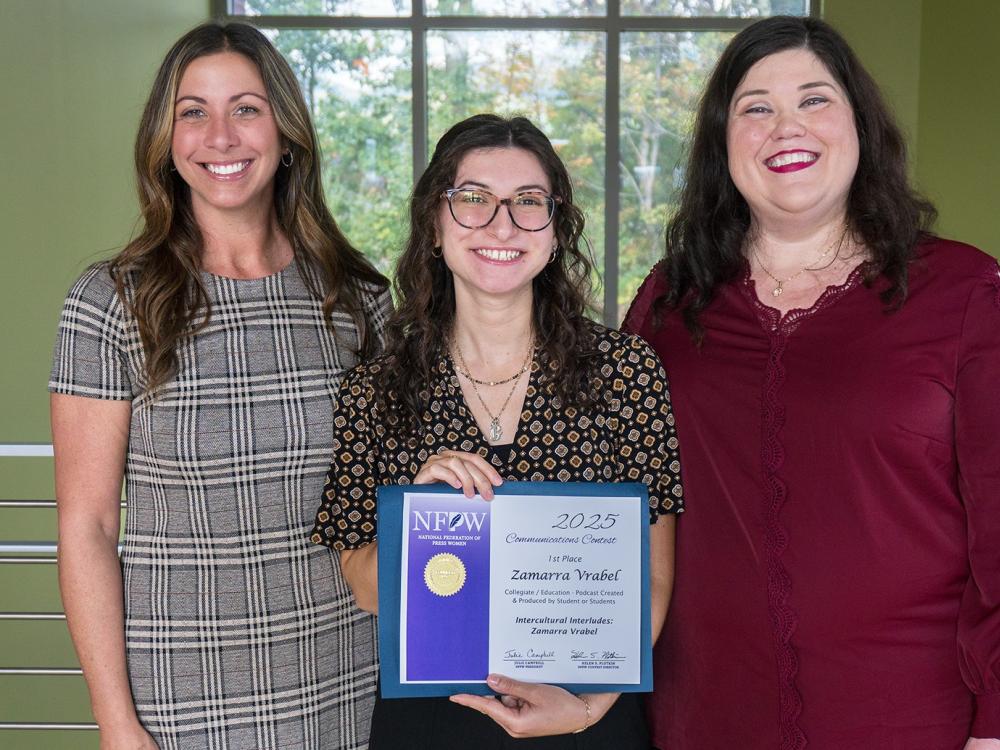 Zamarra Vrabel shows her award certificate, standing between her two female professors, all are smiling