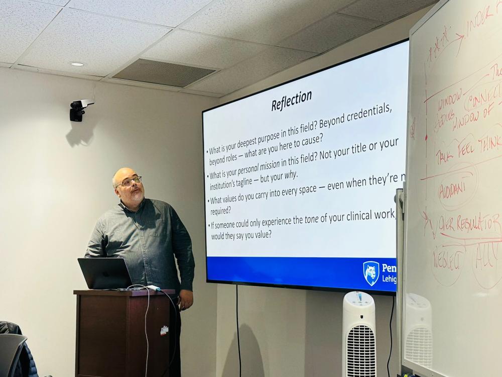 Anibal Torres teaching at a podium next to a projected presentation.