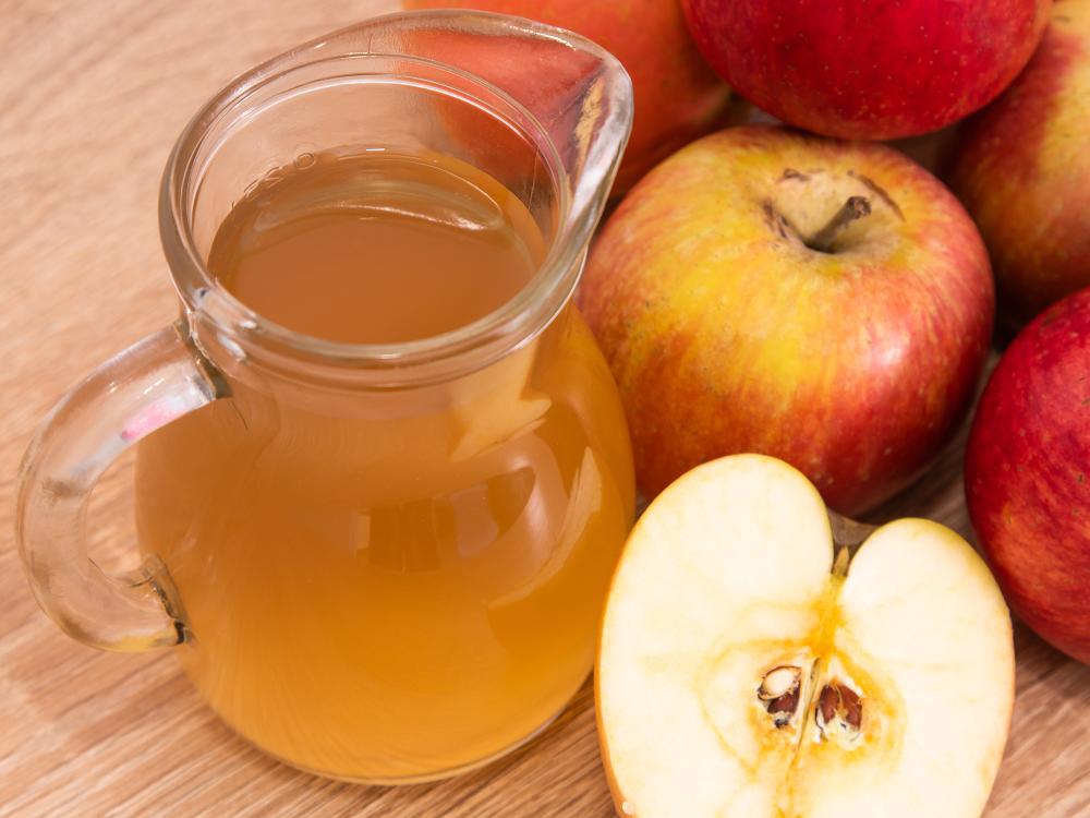 a glass jug of apple cider next to a pile of apples