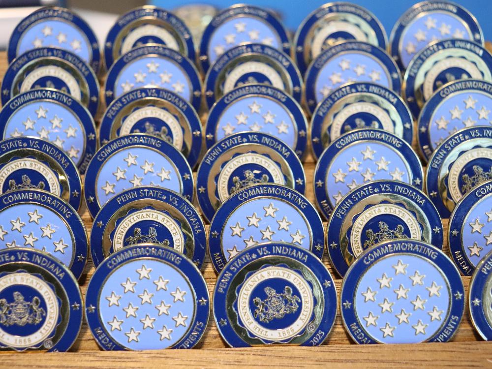 Metal coins with the Penn State logo and white stars on a light blue background.