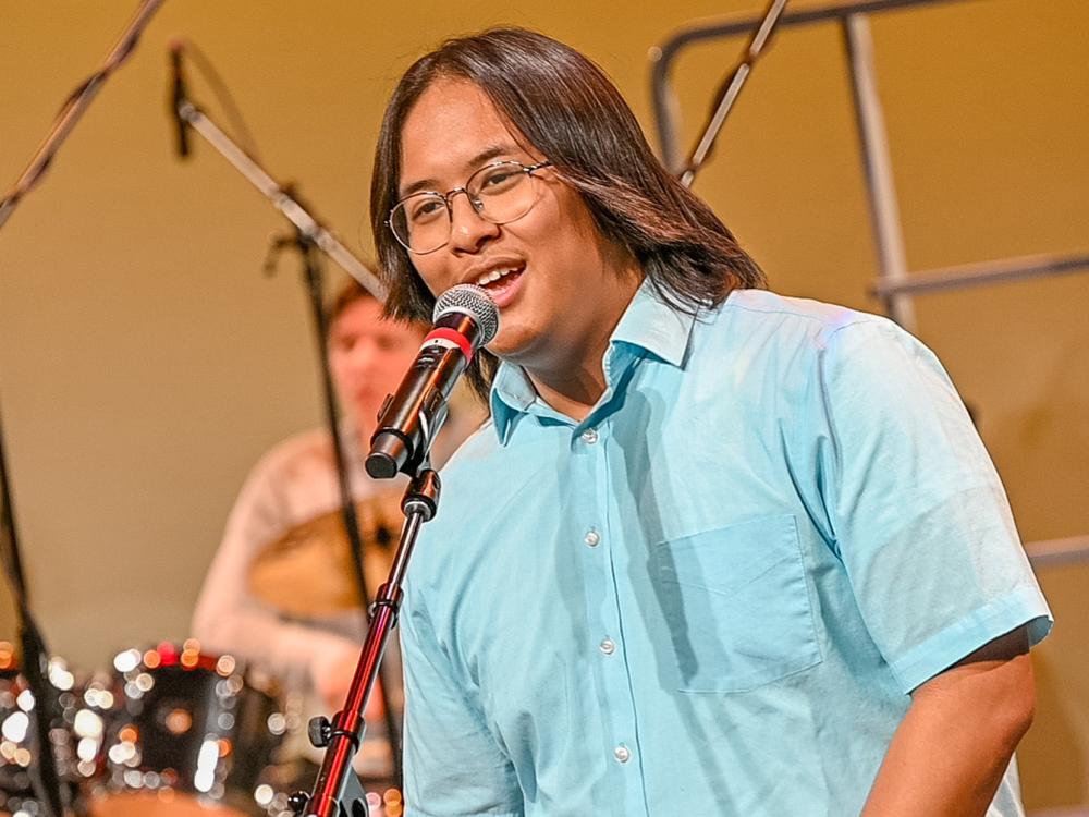 A student sings into a microphone on stage during a campus concert