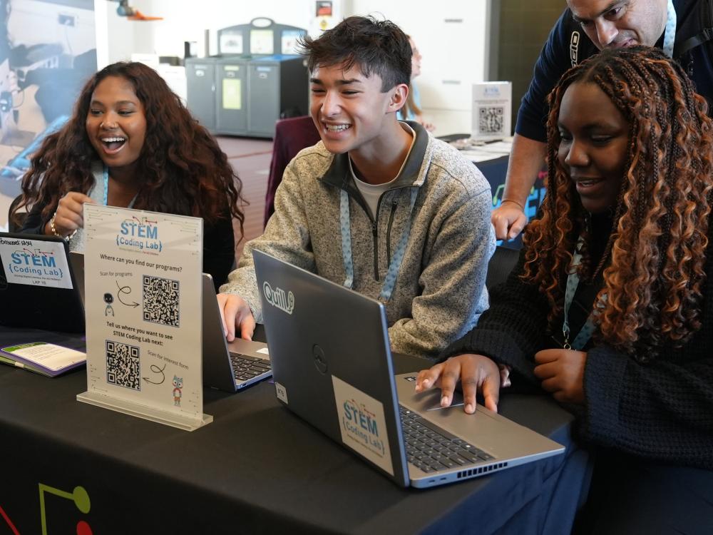 Three students sitting at a table with laptops.