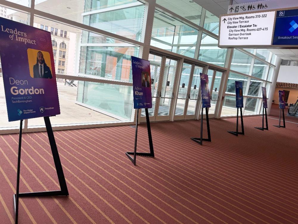 Colorful Leaders of Impact posters line a hallway at The Global Impact Forum, featuring speaker names and photos.
