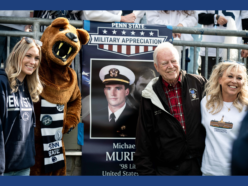 Three people pose with the Nittany Lion mascot in front of a banner.