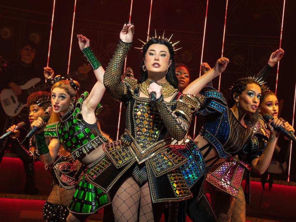 A diverse cast of women wear Tudor revival costumes and hold microphones.