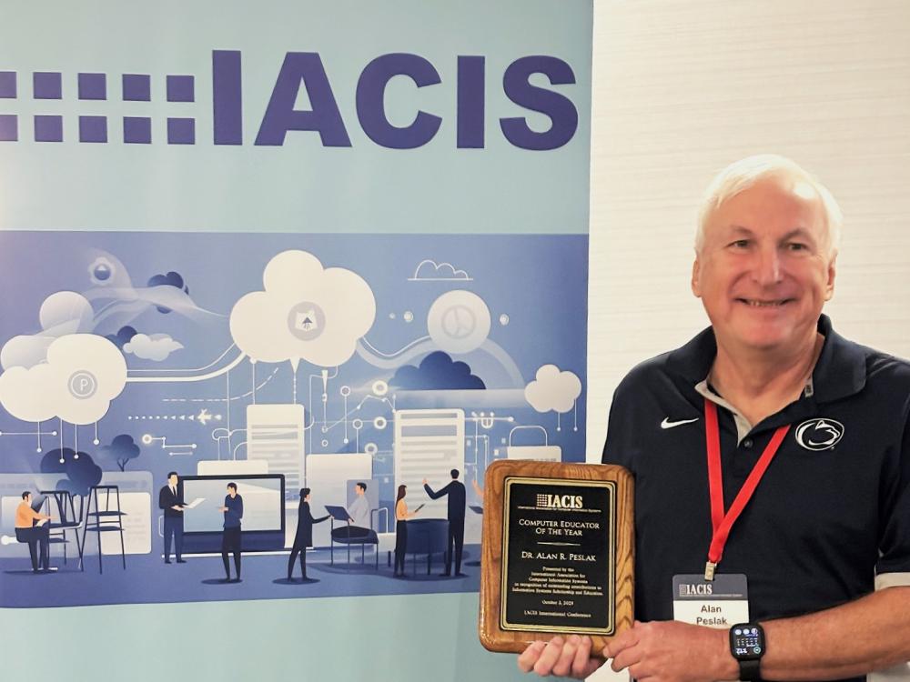 Person poses for a photo holding a IACIS Educator of the Year Award in front of an IACIS banner