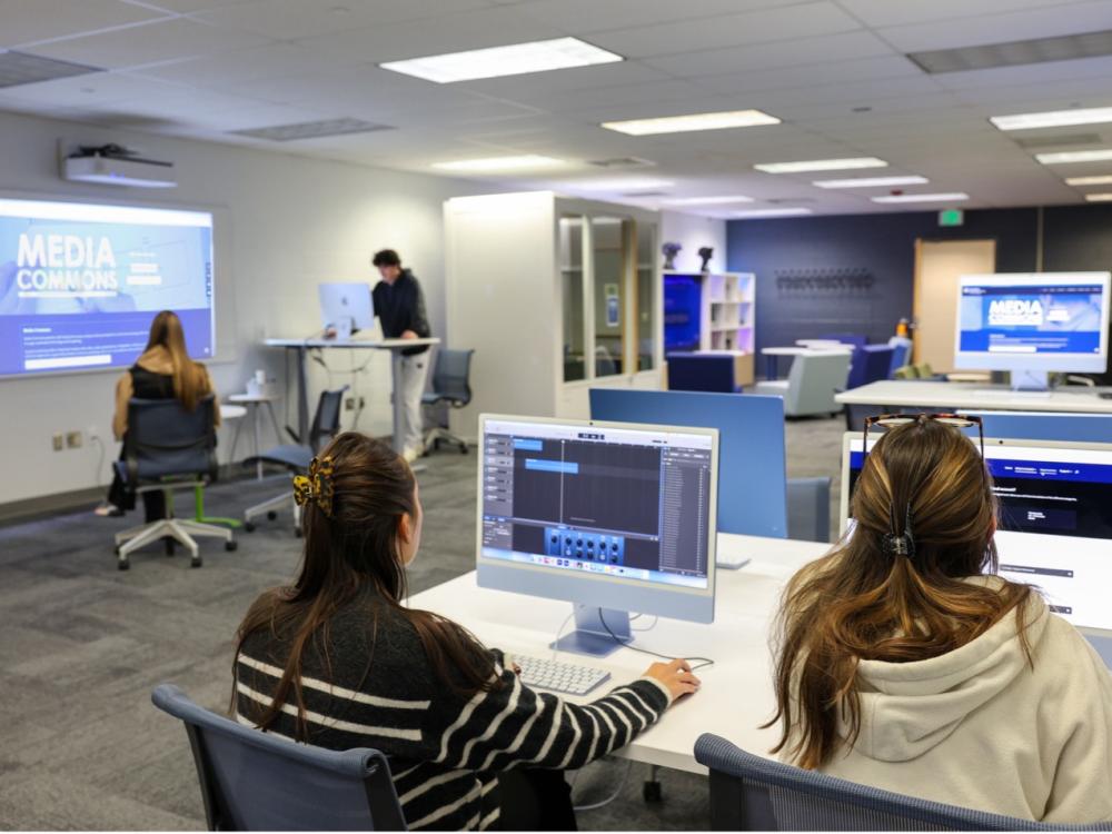 Bright room with four students working at computer stations.