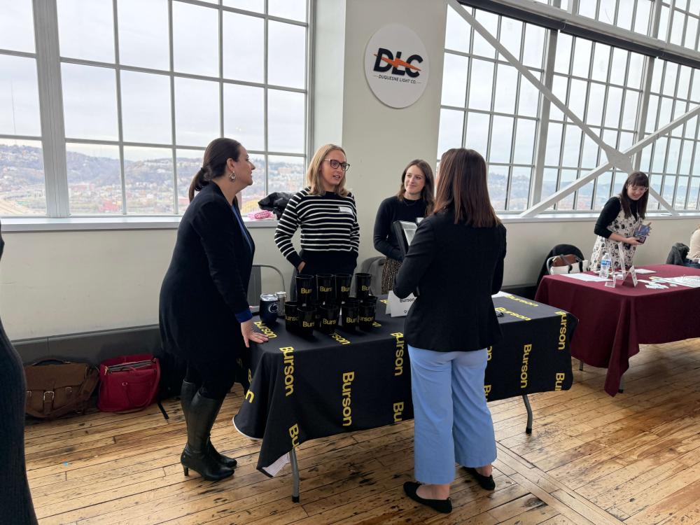 People collecting information at an exhibit table in front of a glass window