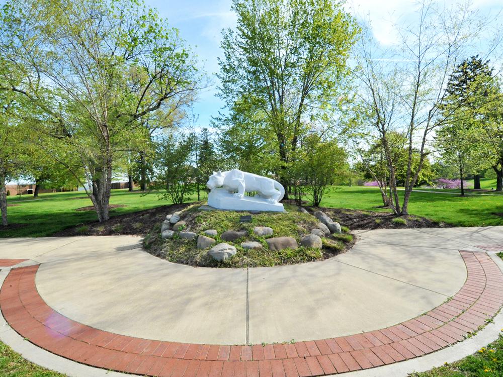 A photo of the Lion Shrine at Penn State Beaver which sits atop a mound and is surrounded by landscaping