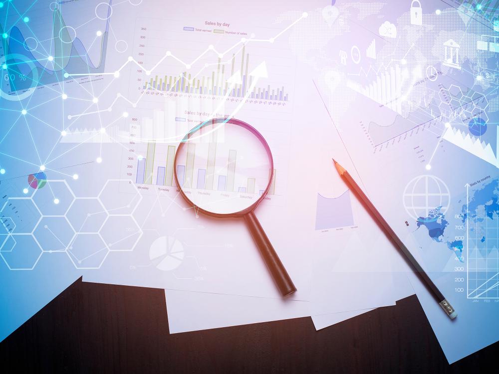 Magnifying glass and pencil on printed charts with digital overlays of graphs and maps representing global data and analytics.