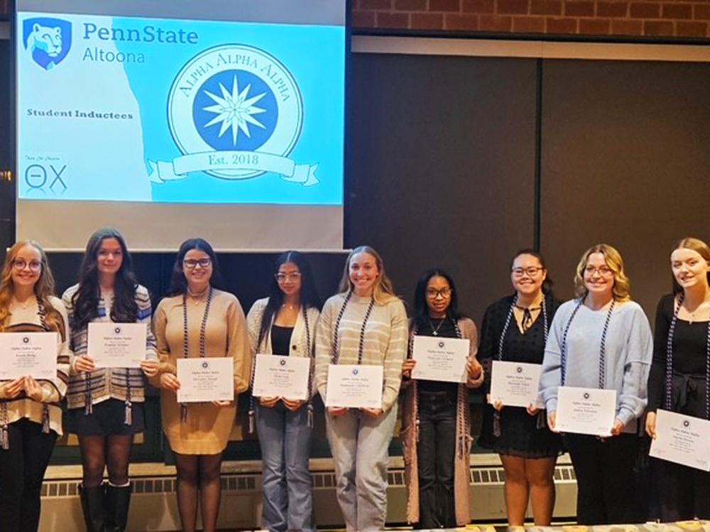 A group of Penn State Altoona students stand in a row holding certificates during the Tri-Alpha Honor Society induction ceremony.