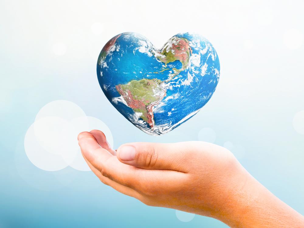Hand holding a heart-shaped Earth against a soft blue background, symbolizing global love, kindness, and environmental care.