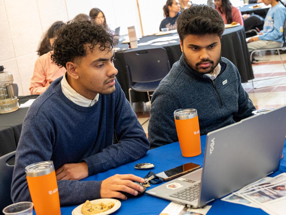 Two students look at a laptop during a luncheon