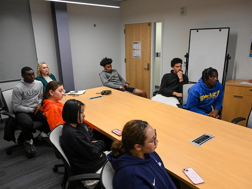 A group of students and an adviser sit around a long table listening to a presentation