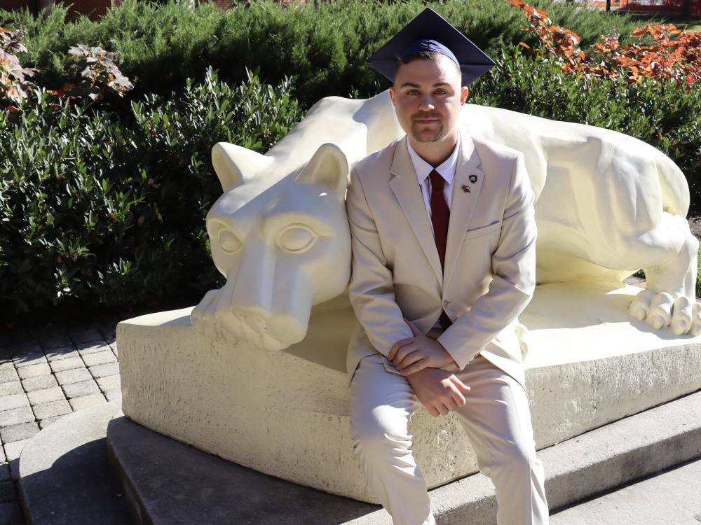 Bailey McCloskey wearing a graduation cap, sitting by the Lion statue