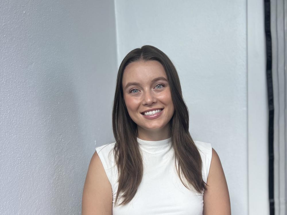 White young woman with brown hair smiling while wearing black pants and white shirt